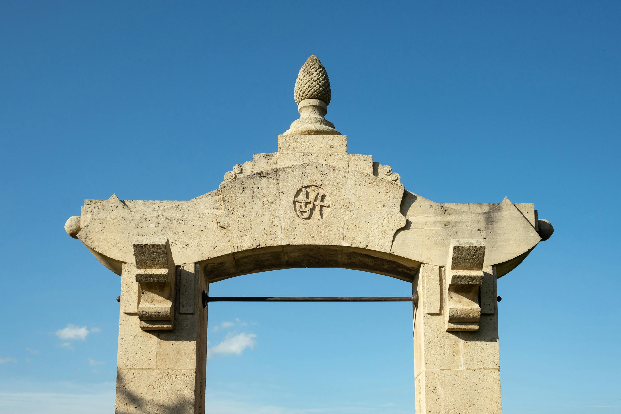 Elegant stone archway with decorative top, captured against a clear blue sky in France.